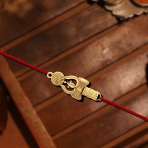 A beautifully handcrafted Trishul Rakhi made of 92.5 hallmarked silver, featuring an intricate trishul design on a vibrant red thread, displayed on a wooden background.