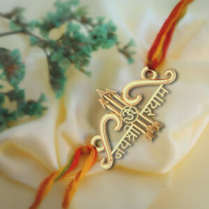 A beautifully handcrafted silver Ram Rakhi with intricate design featuring bows and arrows, with Jai Shree Shyam handcrafted, placed on a soft, off-white fabric background with green foliage.